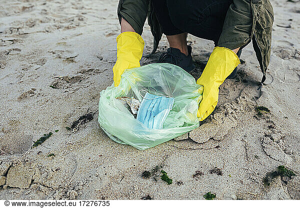 Frau sammelt Einweggesichtsmaske in Müllsack bei Strandreinigung