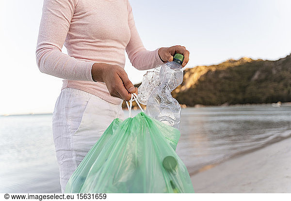 Frau sammelt leere Plastikflaschen am Strand