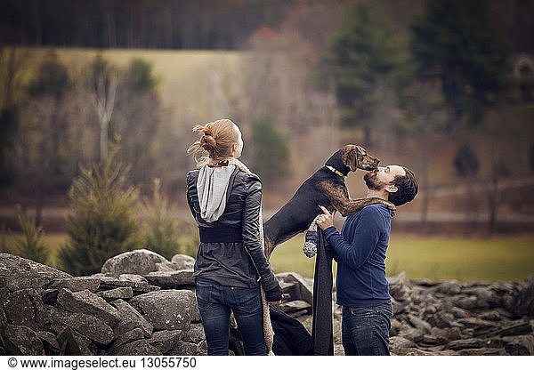 Frau schaut Mann spielt mit Hund an Steinmauer