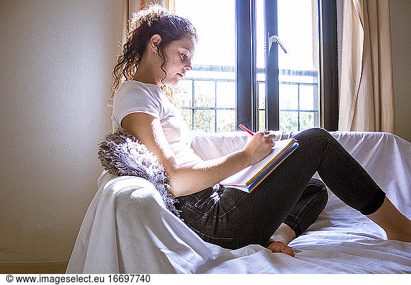 Frau schreibt in einem Notizbuch auf einem weißen Sofa vor einem Fenster