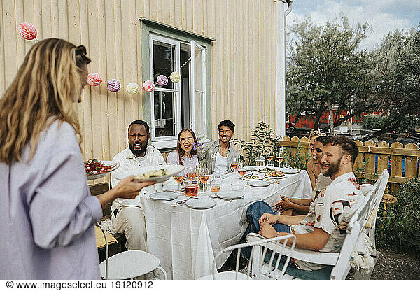 Frau serviert Essen an männliche und weibliche Freunde während einer Dinnerparty im Café