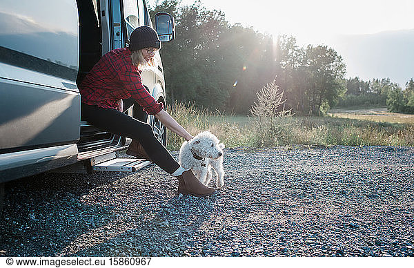 Frau sitzt auf einem Wohnmobil und streichelt beim Camping ihren Hund