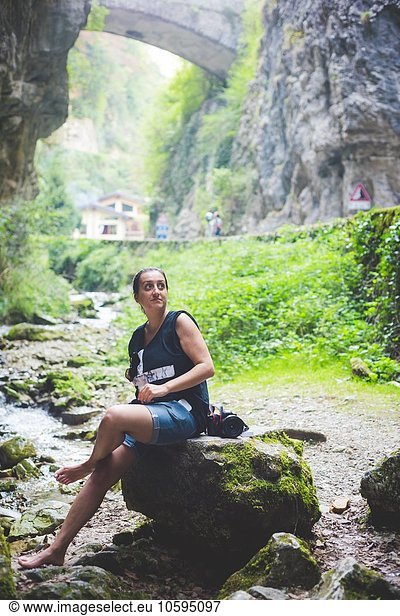 Frau sitzt auf Felsen im Bach  Felshügel und Steinbrücke im Hintergrund  Garda  Italien