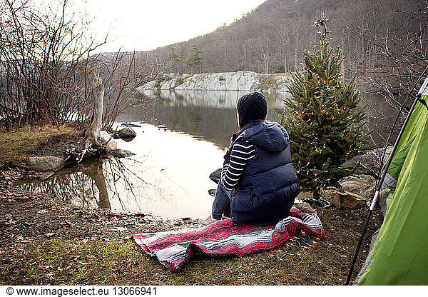 Frau sitzt auf Handtuch am Seeufer bei Kiefer