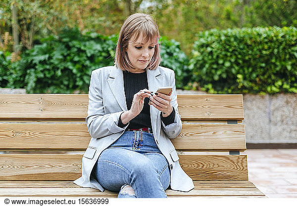 Frau sitzt auf Parkbank und benutzt Mobiltelefon