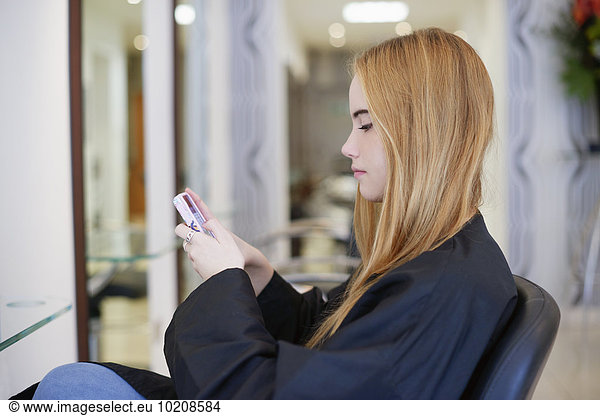 Frau SMS mit Handy im Friseursalon