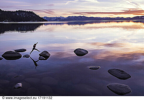 Frau springt bei Sonnenuntergang am Lake Tahoe von Fels zu Fels