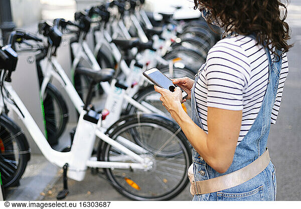Frau steht in der Nähe eines Fahrradständers und benutzt ein Smartphone in der Stadt
