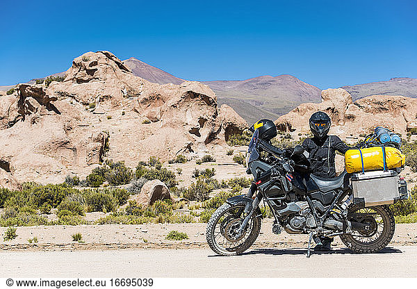 Frau steht neben einem Tourenmotorrad auf einer staubigen Straße in Bolivien