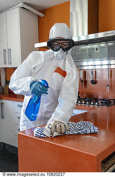 Frau trägt Schutzkleidung  desinfiziert ihre Küche