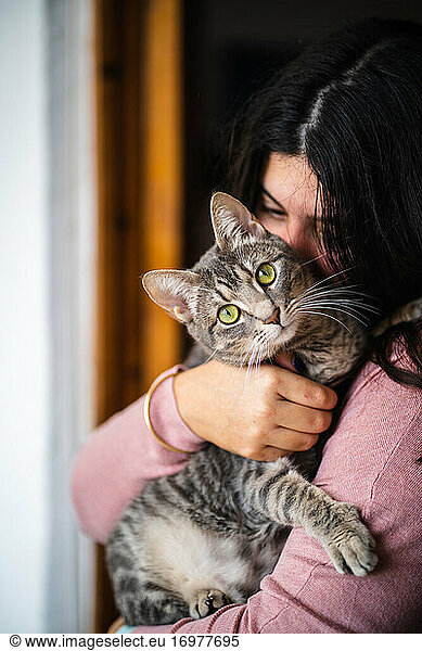 Frau umarmt eine Katze auf ihren Armen. Katze schaut in die Kamera