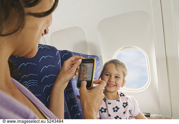 Frau und Mädchen mit Handy im Economy Class Airliner