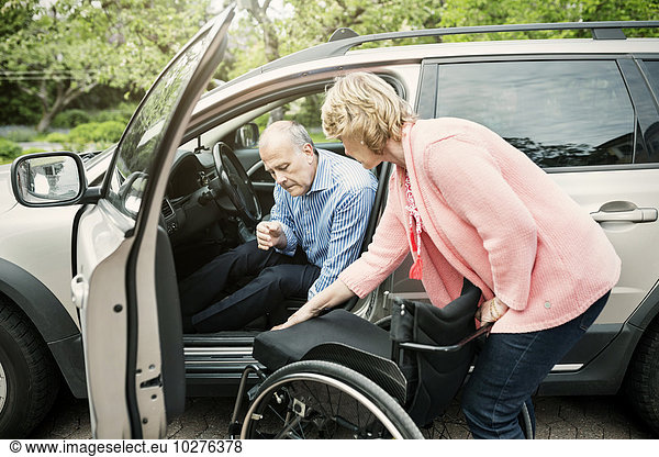 Frau unterstützt behinderten Mann beim Aussteigen aus dem Auto
