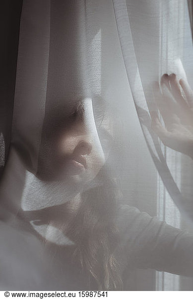 Frau versteckt sich hinter weißem Vorhang