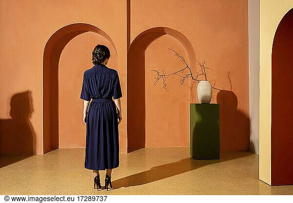 Frau vor einer orangefarbenen Wand mit Bögen stehend
