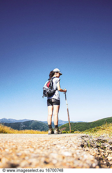 Frau wandert auf Straße gegen Berglandschaft und blauen Himmel