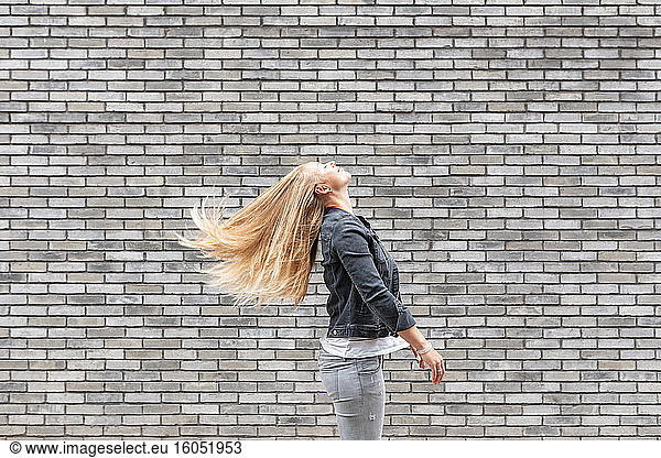 Frau wirft langes Haar  während sie an einer grauen Backsteinmauer steht
