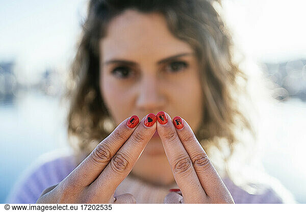 Frau zeigt Alphabete auf Fingernägeln gegen den Himmel