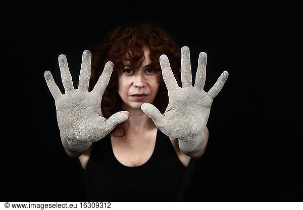 Frau zeigt ihre mit weißem Staub bedeckten Hände vor schwarzem Hintergrund