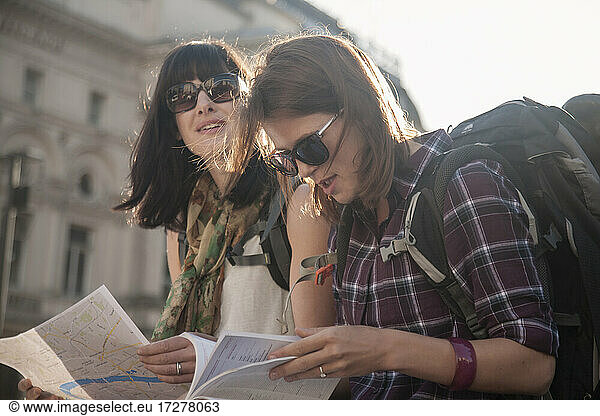 Frauen im Urlaub  die auf dem Stadtplatz sitzend eine Karte lesen