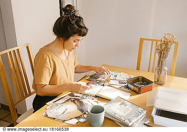 Freelancer arranging paper clippings in book on desk at home