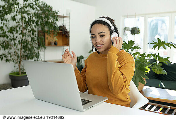 Freelancer doing video call over laptop using wireless headphones at home office