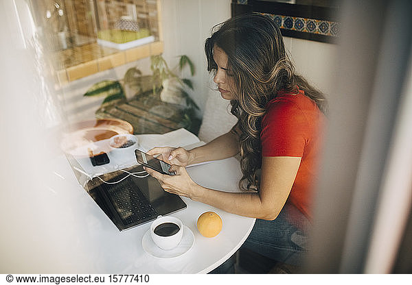 Freelancer female using phone seen through glass window