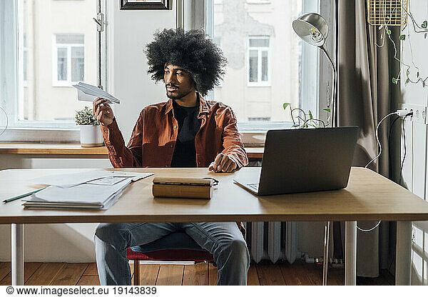 Freelancer holding paper plane sitting on desk at home