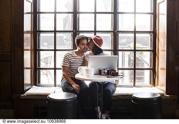 Freelancer kissing man while using laptop at cafe