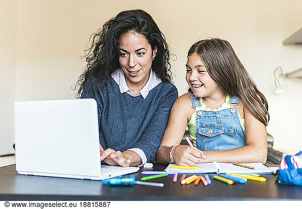 Freelancer mother showing daughter over laptop at table