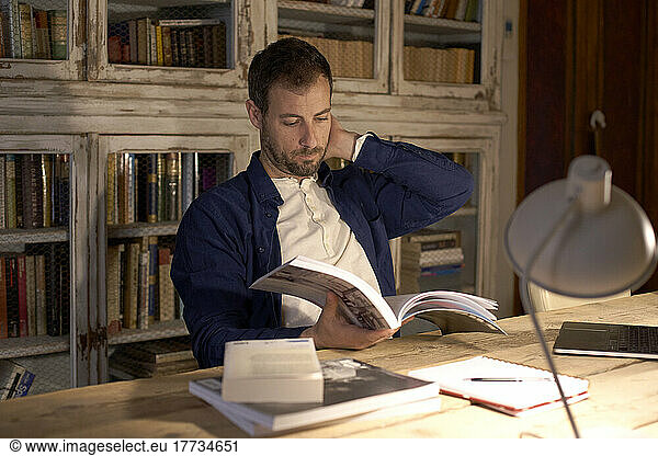 Freelancer reading book at desk in home office