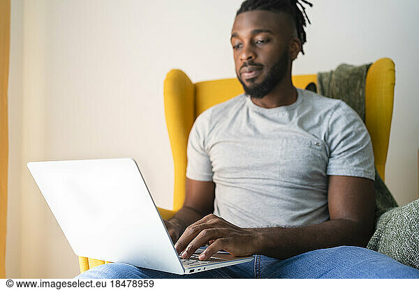Freelancer sitting on armchair and using laptop at home