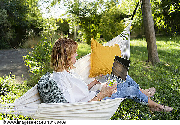 Freelancer sitting with laptop in hammock at garden