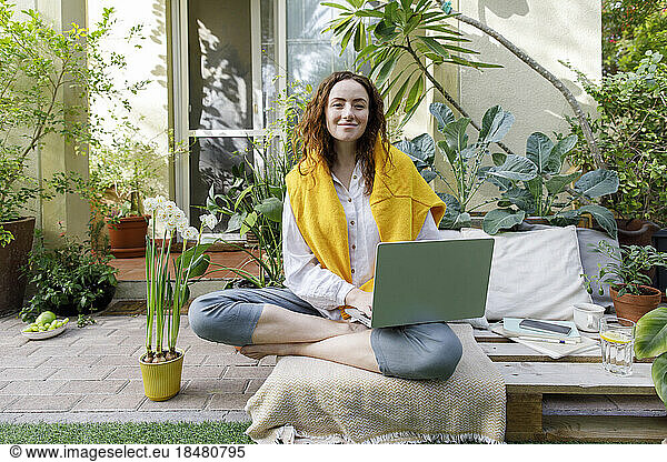 Freelancer sitting with laptop on wooden crate at backyard