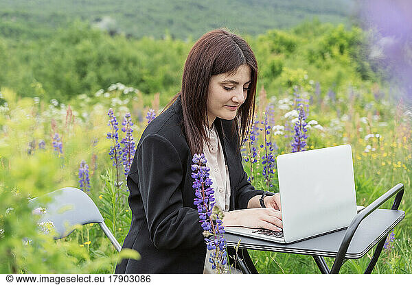 Freelancer using laptop on desk surrounded by flowers