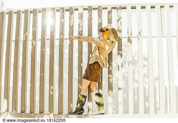 Freelancer wearing bird mask standing on stripped wall