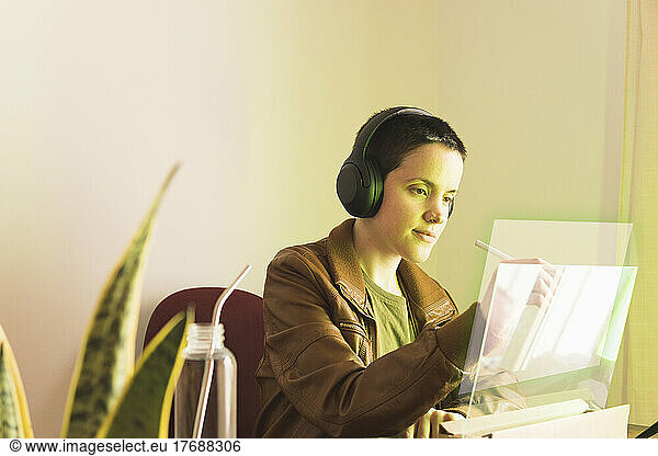 Freelancer wearing headphones writing on transparent screen with digitized pen
