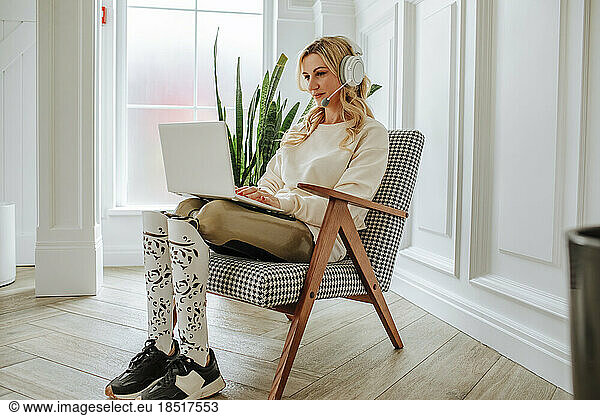 Freelancer with artificial limb wearing headset and working on laptop at home
