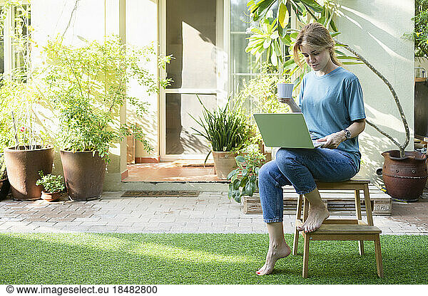 Freelancer with coffee cup and laptop sitting in garden