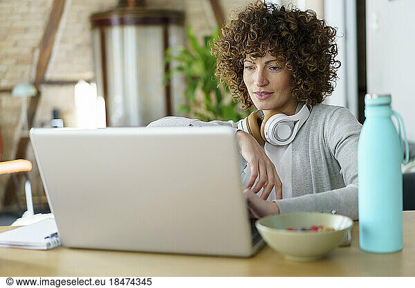 Freelancer with curly hair using laptop at desk in home