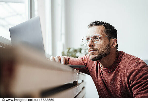 Freelancer with eyeglasses working through laptop at home