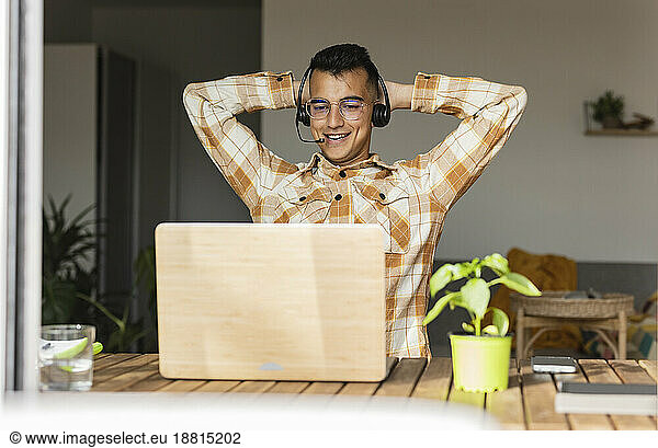 Freelancer with hands behind head doing video call at home office