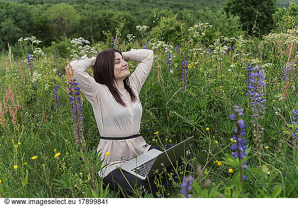 Freelancer with laptop relaxing amidst flowers in meadow