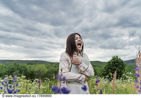 Freelancer with laptop shouting amidst lupine flowers