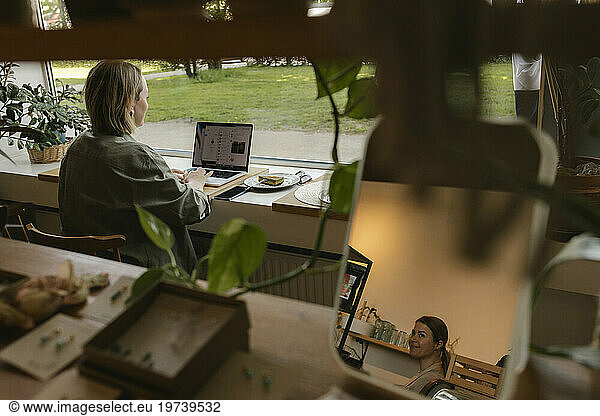 Freelancer working with laptop and owner's reflection in mirror at cafe