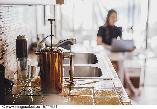 French press on wet kitchen counter while woman working in background