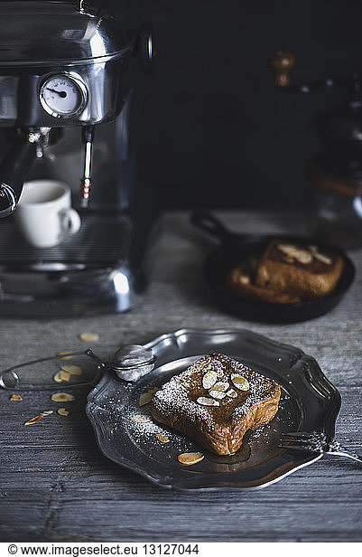 French toasts with almonds served in plate by espresso maker on wooden table