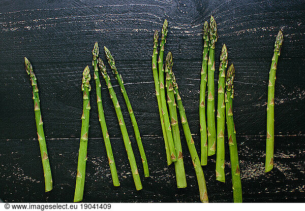 Fresh cut asparagus spears lay on a black painted rustic wooden table