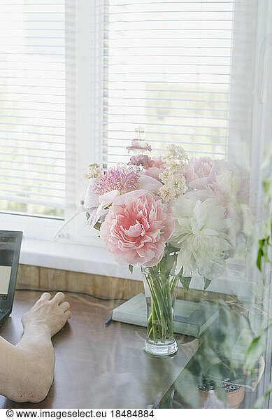 Fresh flowers in vase by freelancer at desk