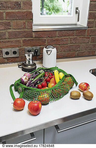 Fresh fruits and vegetables in reusable shopping bag on kitchen counter at home